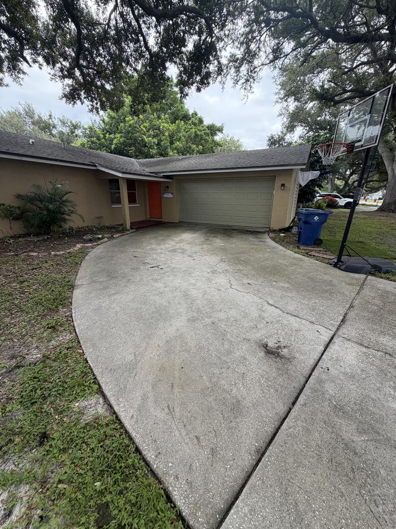 Driveway concrete tan with ground-in dirt and a dark stain before washing