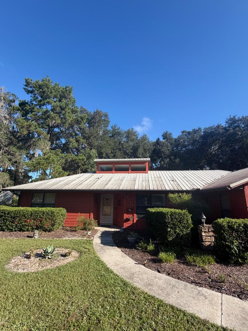 Red single-story house from the front walk with a dull, dark-streaked metal roof
